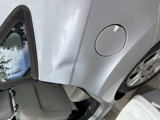 Silver rear quarter panel with a dent above the fuel door